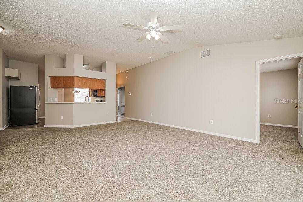 A carpeted living room features a ceiling fan and an open view into the kitchen — 11025 WHITTNEY CHASE DRIVE, RIVERVIEW, FL