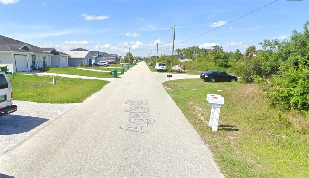A paved residential street features houses on the left and a wooded lot on the right — 8518 AGATE STREET, PORT CHARLOTTE, FL