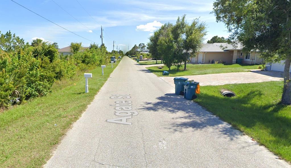 A paved residential street with mailboxes, trash bins, and houses on a sunny day — 8518 AGATE STREET, PORT CHARLOTTE, FL