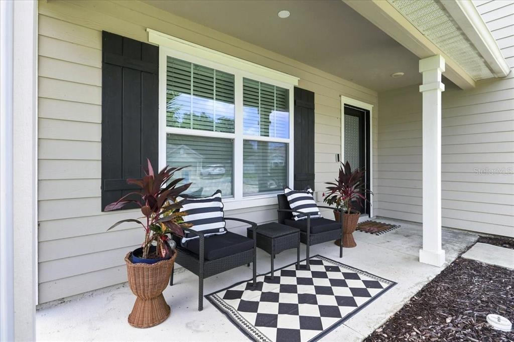 A covered front porch features two black chairs, a small table, and a checkered rug — 22885 NW 197TH PLACE, HIGH SPRINGS, FL