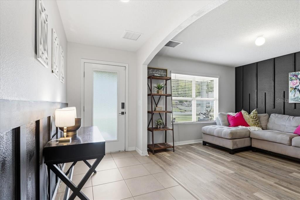 A living room with wood-look flooring, a black accent wall, and a tiled entryway — 22885 NW 197TH PLACE, HIGH SPRINGS, FL