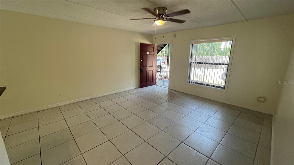 An empty room features light-colored floor tiles, a ceiling fan, and an open exterior door — 2800 E 113TH AVENUE UNIT B2113, TAMPA, FL