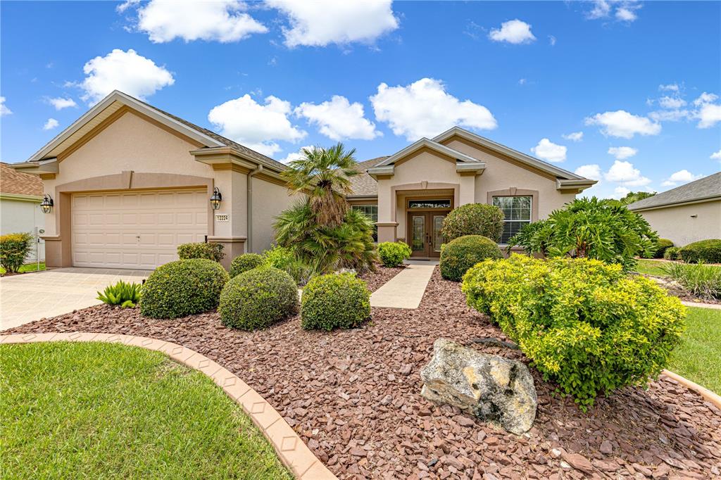 A single-story suburban house with a tan stucco exterior, a two-car garage, and landscaped yard — 12224 SE 91ST AVENUE, SUMMERFIELD, FL
