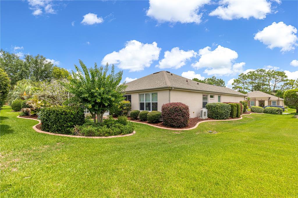The exterior of a beige stucco house features a landscaped yard with shrubs and trees — 12224 SE 91ST AVENUE, SUMMERFIELD, FL