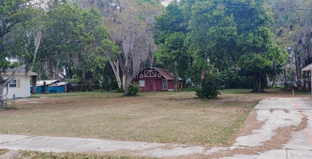 A red barn-style shed sits in a grassy yard behind a house and trees — 564 SW OAK AVENUE W, SEBRING, FL