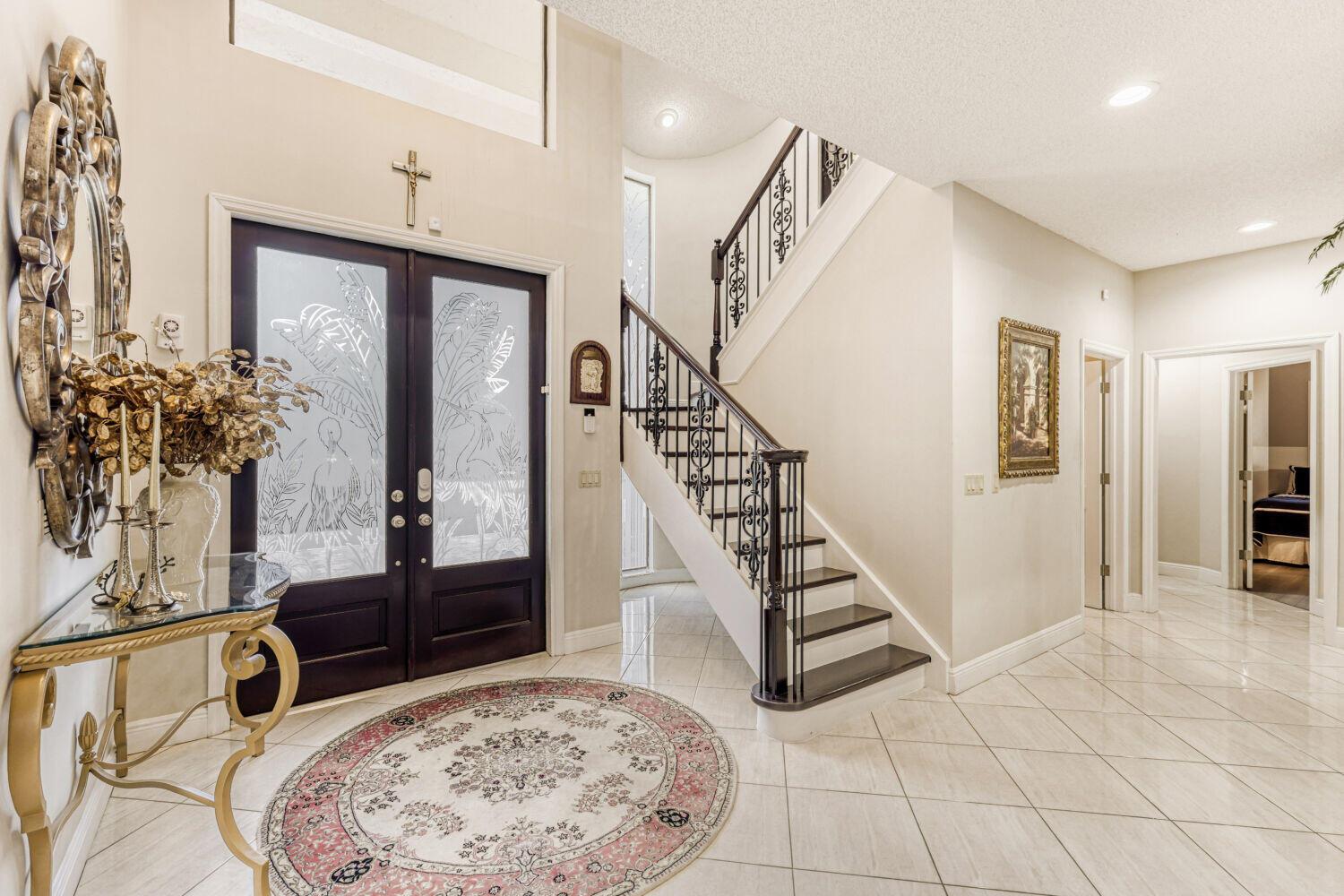 A bright foyer features a grand staircase, tiled floors, and double doors with etched glass — 10273 St Andrews Road, Boynton Beach FL 33436, BOYNTON BEACH, FL