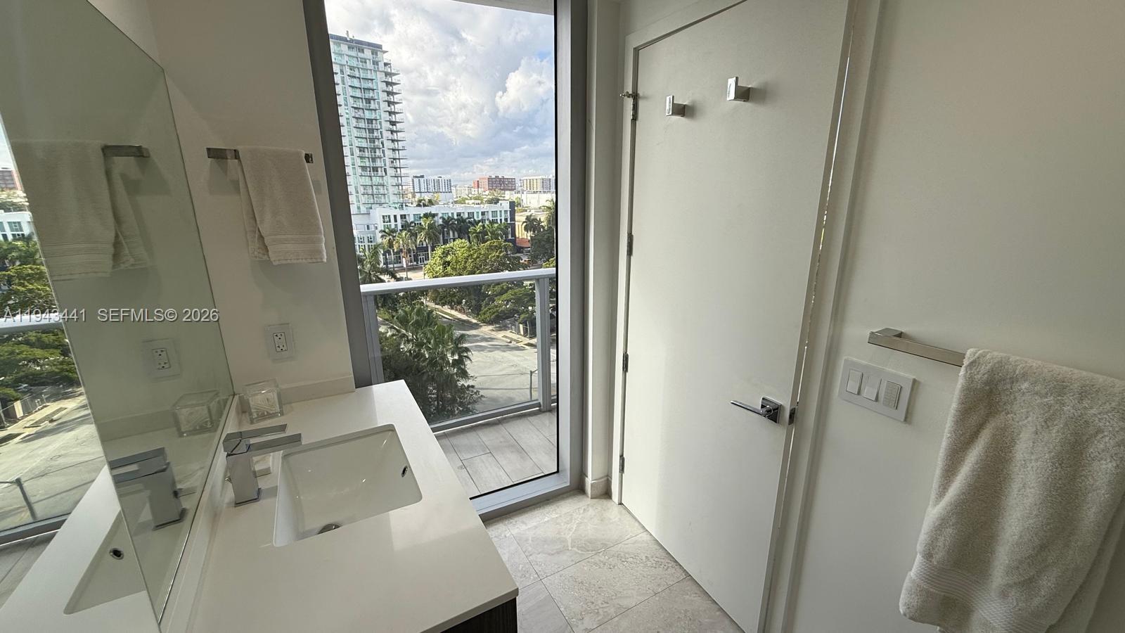 A modern bathroom features a white vanity, a large mirror, and a balcony with city views — 488 NE 18th St # 700, Miami FL 33132, MIAMI, FL