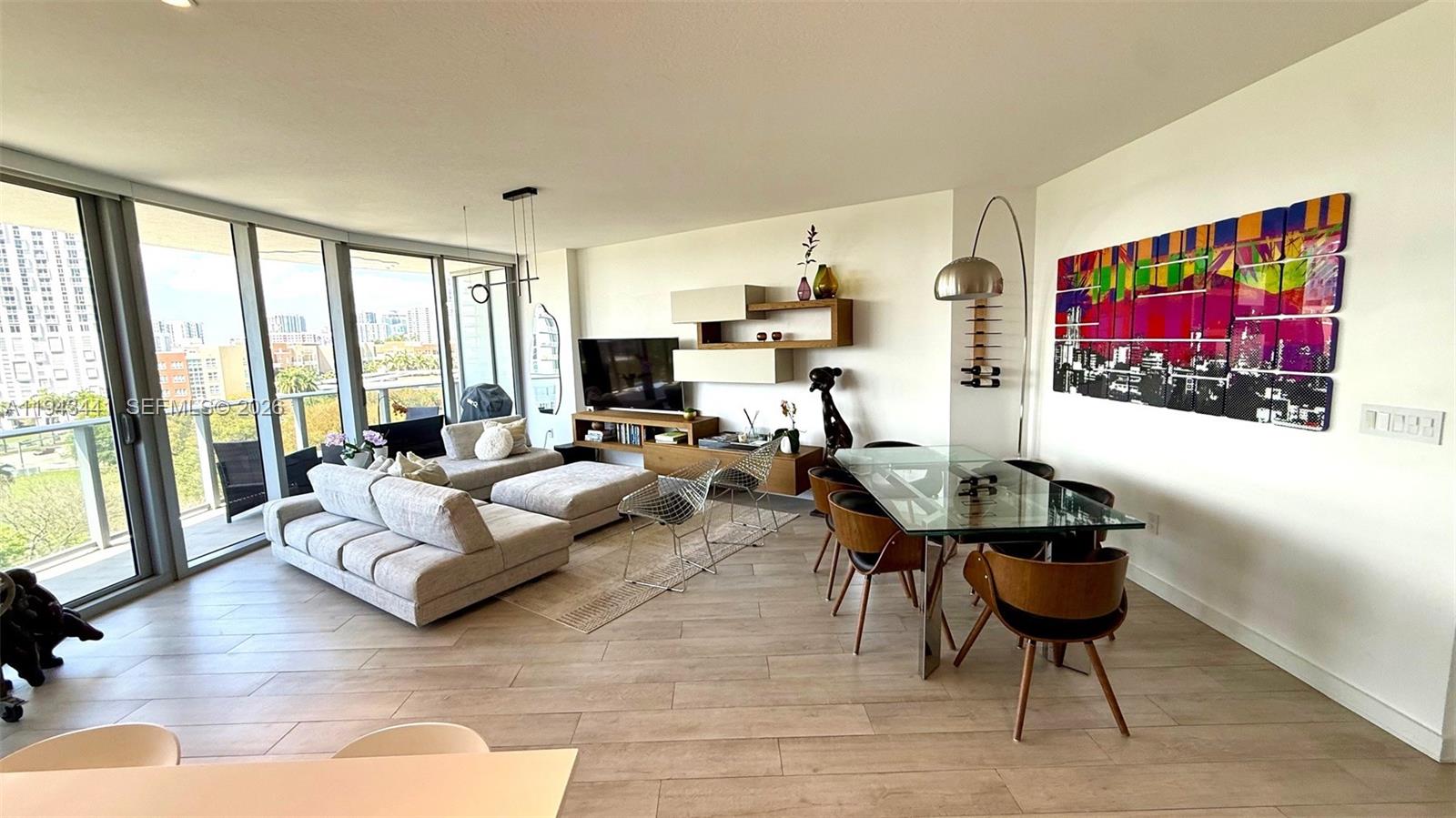 A modern living and dining area features light wood flooring, floor-to-ceiling windows, and contemporary furniture — 488 NE 18th St # 700, Miami FL 33132, MIAMI, FL