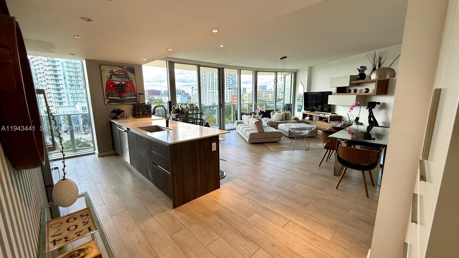 An open-concept condo features a modern kitchen island, living area, and floor-to-ceiling windows — 488 NE 18th St # 700, Miami FL 33132, MIAMI, FL
