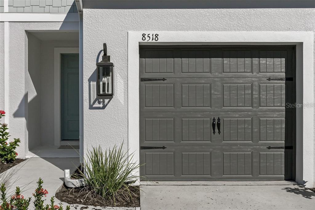 A gray garage door with decorative hardware sits beside a front entrance with a lantern — 8518 CANYON CREEK TRAIL, PARRISH, FL