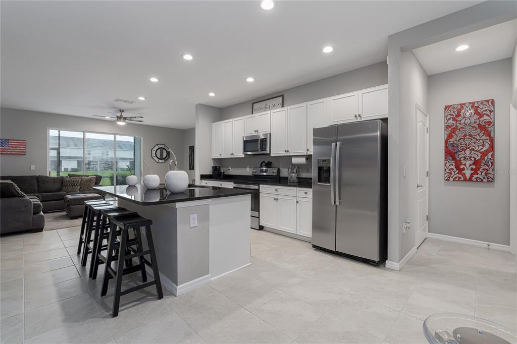 A kitchen with white cabinets, stainless steel appliances, and a black-topped island with bar stools — 8518 CANYON CREEK TRAIL, PARRISH, FL