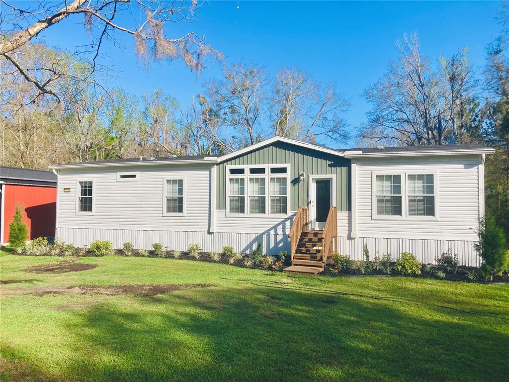 A single-story manufactured home with white siding, a green accent wall, and wooden front steps — 10750 NW 190TH STREET, MICANOPY, FL