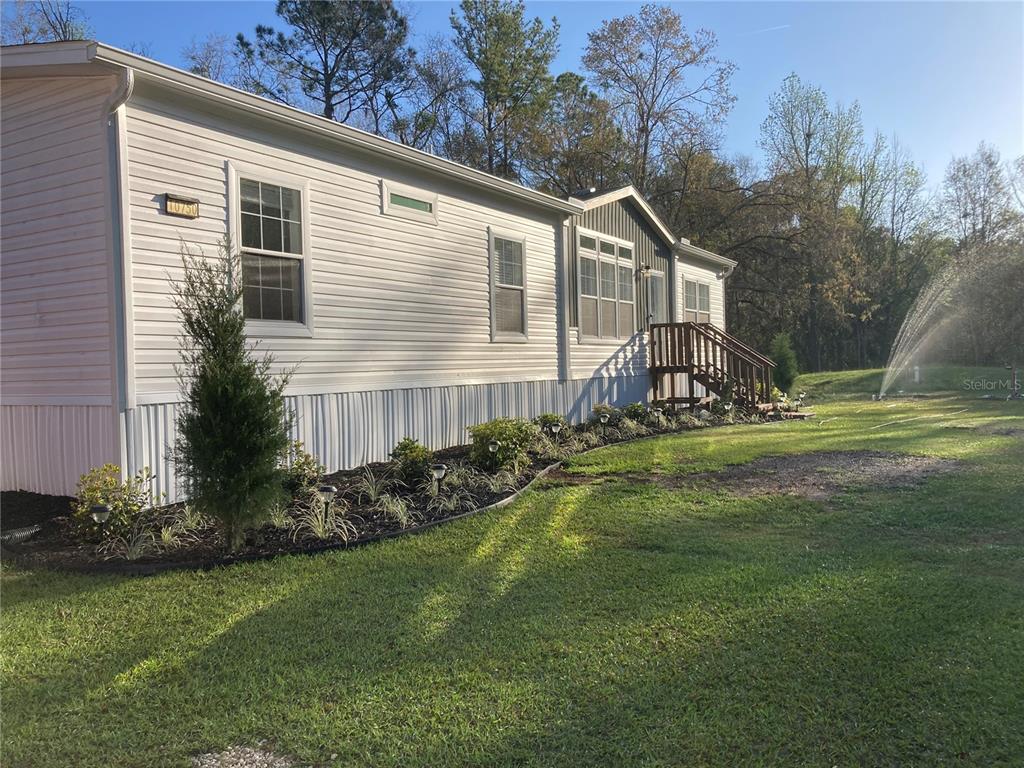 A single-story manufactured home with white siding and a wooden deck sits on a lawn — 10750 NW 190TH STREET, MICANOPY, FL