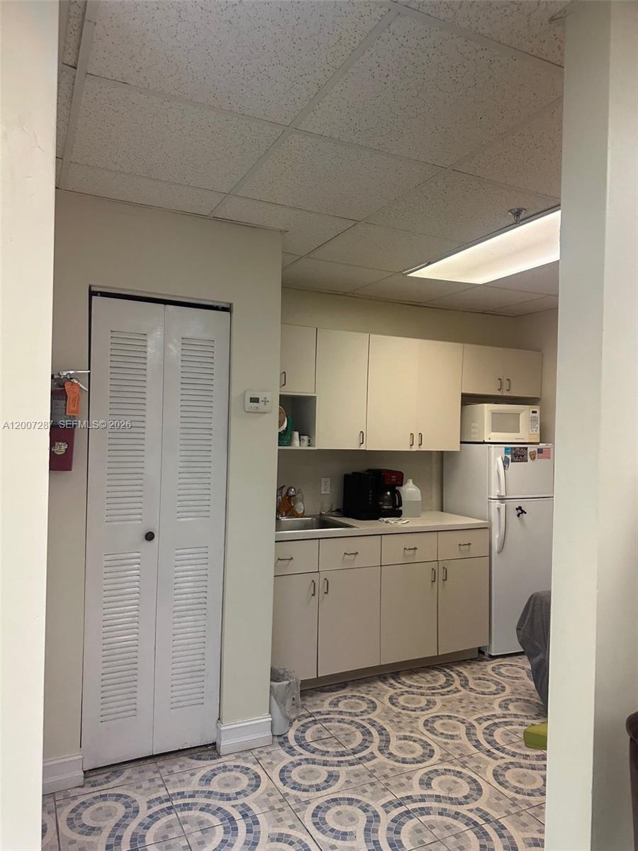 A small kitchen features beige cabinets, a white refrigerator, and patterned tile flooring — 12101 NW 98th Ave, Hialeah Gardens FL 33018, HIALEAH GARDENS, FL