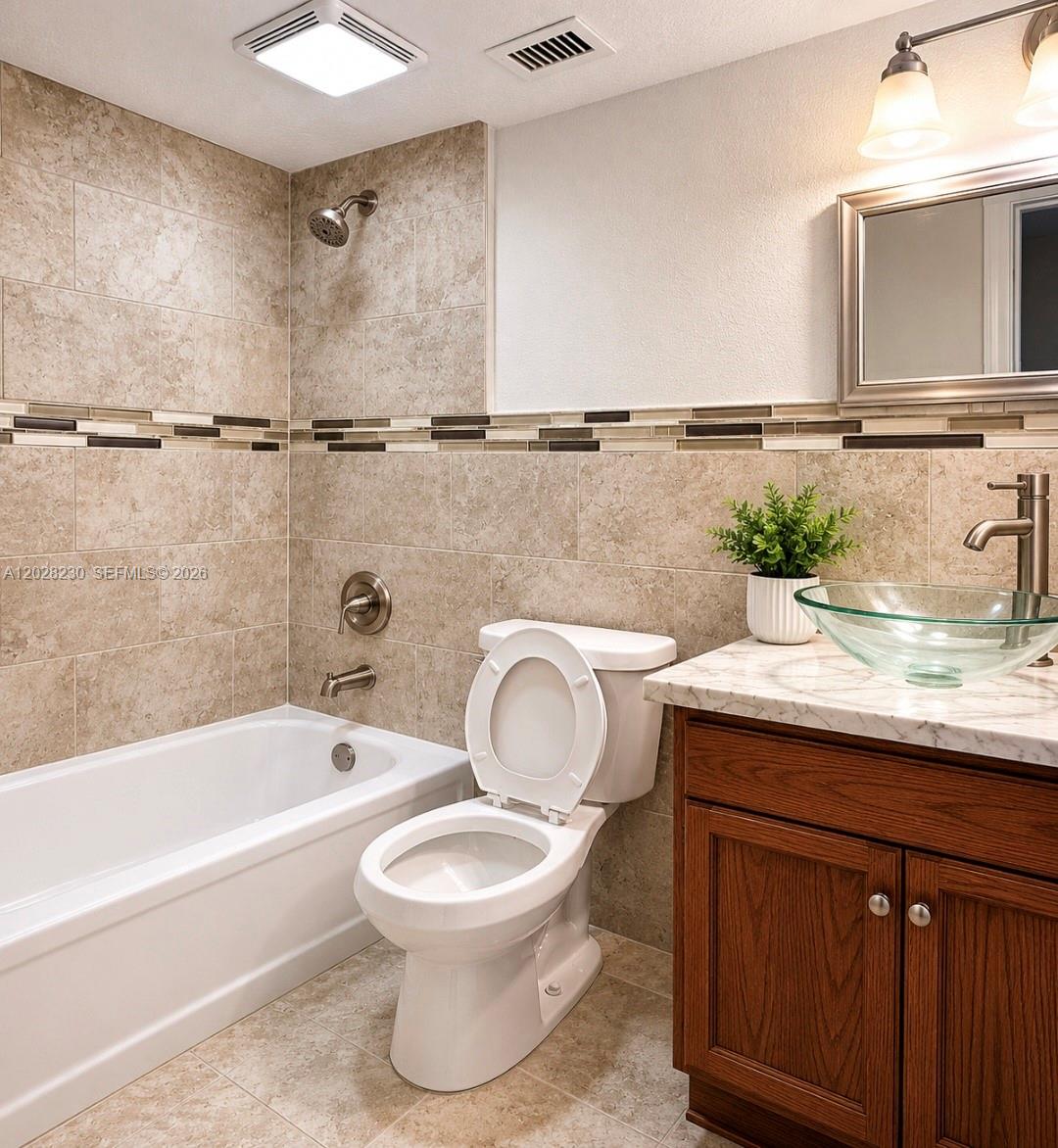 A bathroom features a white bathtub, a toilet, and a glass vessel sink vanity — LAUDERHILL, FL