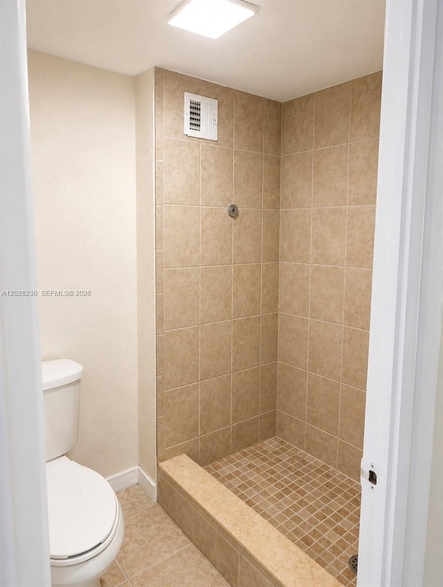 A bathroom features a tiled walk-in shower with a curb next to a white toilet — LAUDERHILL, FL