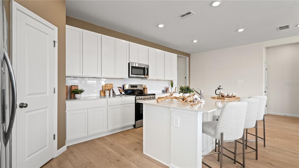 A modern kitchen features white cabinetry, a central island with bar seating, and light flooring — 4578 CORAL HARBOUR ROAD, KISSIMMEE, FL