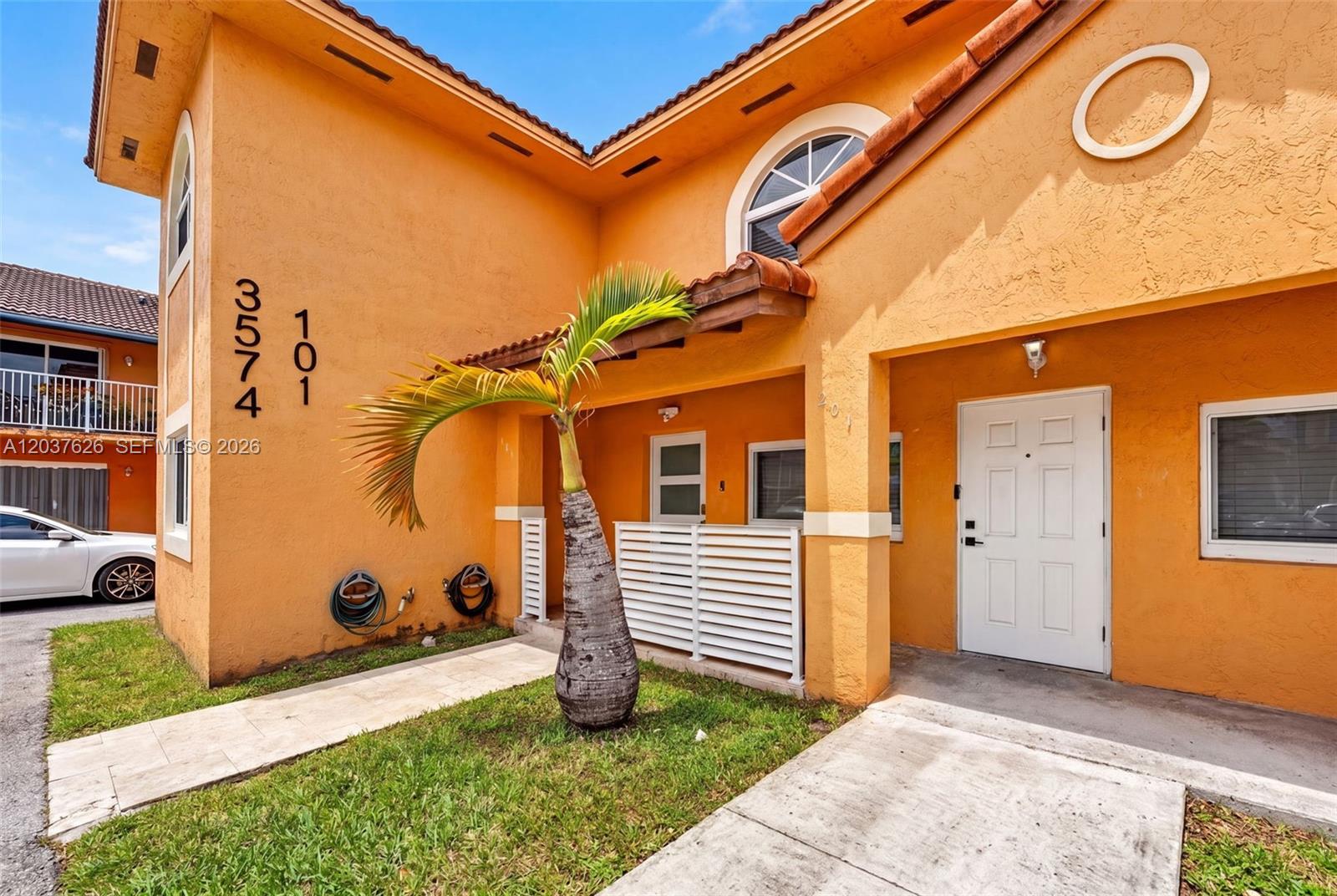 An orange two-story building features a palm tree, white front door, and a small patio — 3574 W 80th St # 201, Hialeah FL 33018, HIALEAH, FL