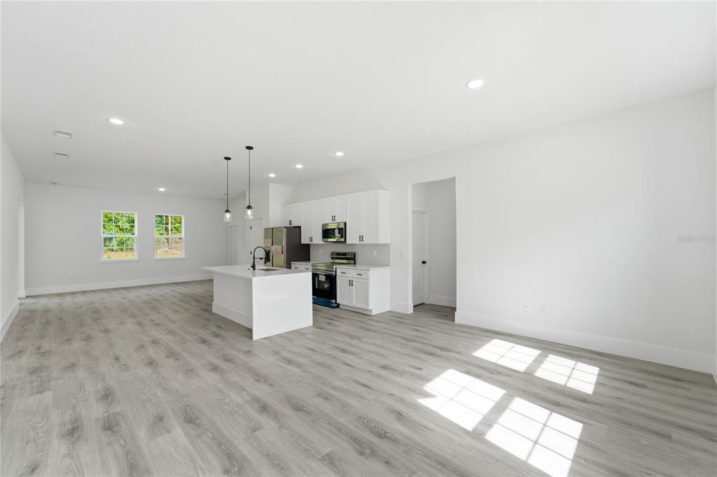 An open-concept kitchen and living area features white cabinets, a central island, and wood-look flooring — 226 E CALDWELL DRIVE, DUNNELLON, FL