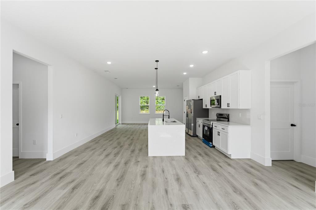A modern kitchen features white cabinets, a central island, and light wood-look flooring — 226 E CALDWELL DRIVE, DUNNELLON, FL
