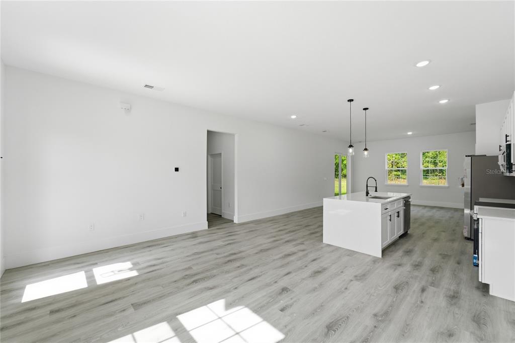 An open-concept kitchen and living area features white cabinetry, a central island, and wood-look flooring — 226 E CALDWELL DRIVE, DUNNELLON, FL
