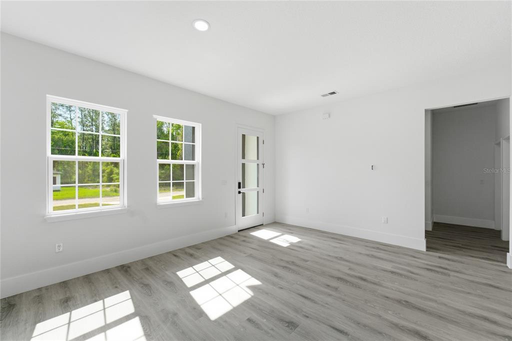 A bright room with white walls, light wood-look flooring, two windows, and a glass-paneled door — 226 E CALDWELL DRIVE, DUNNELLON, FL