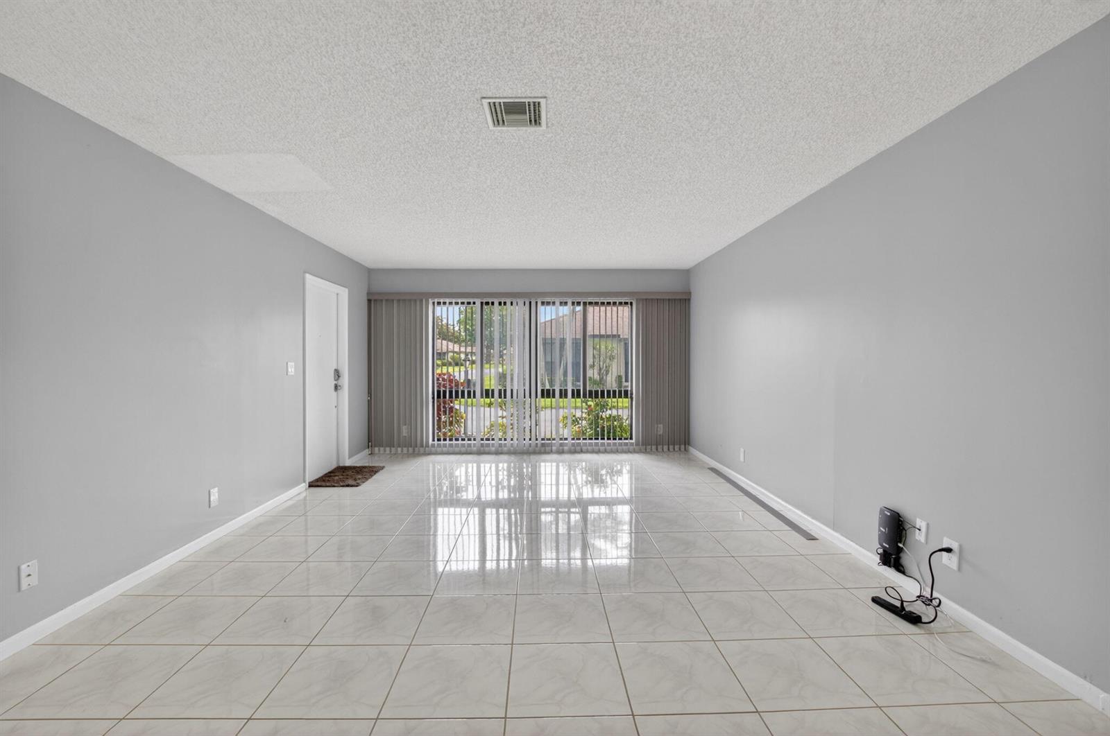 An empty living room features light gray walls, white tile flooring, and large vertical blinds — 4944 Equestrian Circle # A, Boynton Beach FL 33436, BOYNTON BEACH, FL