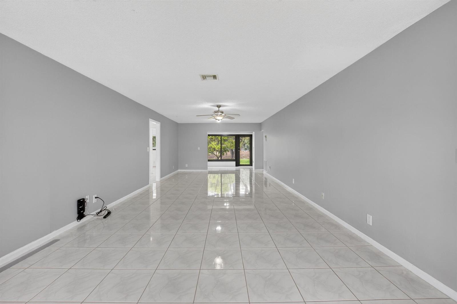 An empty, rectangular living room features gray walls, white tile flooring, and a ceiling fan — 4944 Equestrian Circle # A, Boynton Beach FL 33436, BOYNTON BEACH, FL