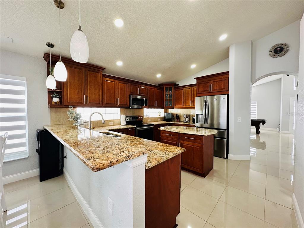 A kitchen features wood cabinets, granite countertops, a stainless steel refrigerator, and tile flooring — 8885 PALISADES BEACH AVENUE, ORLANDO, FL