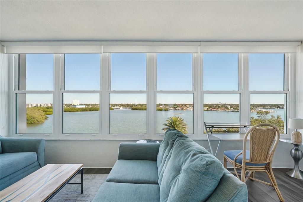 A living room with blue sofas faces a large window wall overlooking a bay — 1847 SHORE DRIVE S UNIT 711, SOUTH PASADENA, FL
