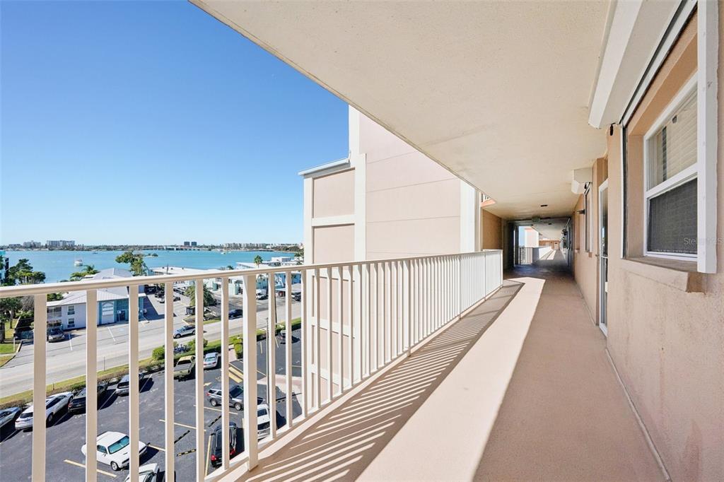 An outdoor balcony with a white railing overlooks a parking lot and a body of water — 1847 SHORE DRIVE S UNIT 711, SOUTH PASADENA, FL