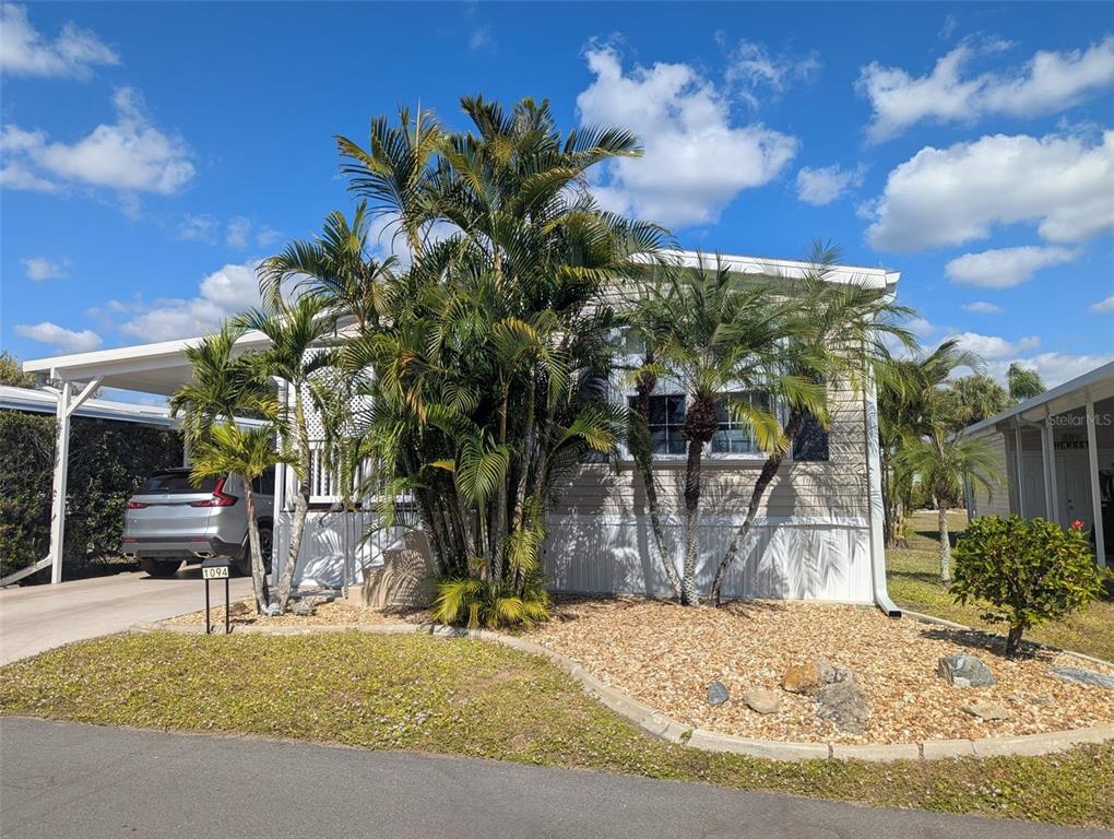A single-story manufactured home with a carport, palm trees, and a gravel front yard — 2100 KINGS HWY UNIT 1094, PORT CHARLOTTE, FL