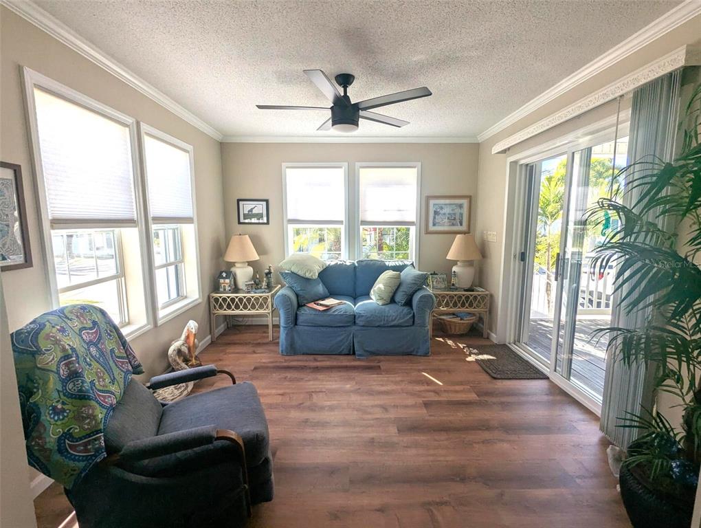 A sunroom features wood-look flooring, a blue sofa, a dark armchair, and sliding glass doors — 2100 KINGS HWY UNIT 1094, PORT CHARLOTTE, FL