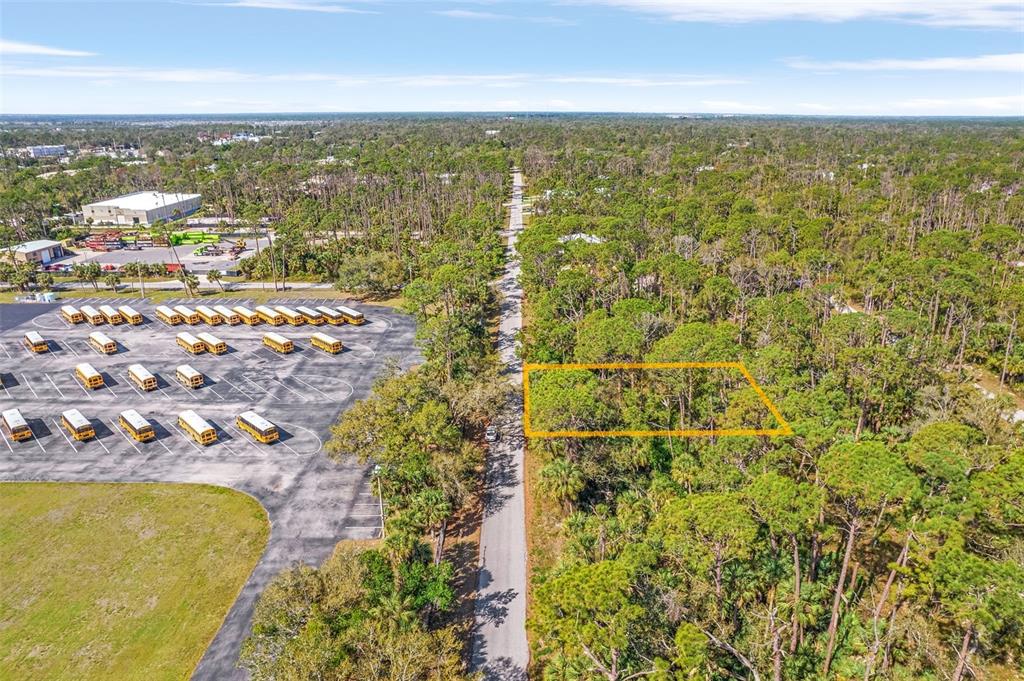 An aerial view shows a wooded lot outlined in yellow next to a school bus parking lot — 17474 GEDDES AVENUE, PORT CHARLOTTE, FL