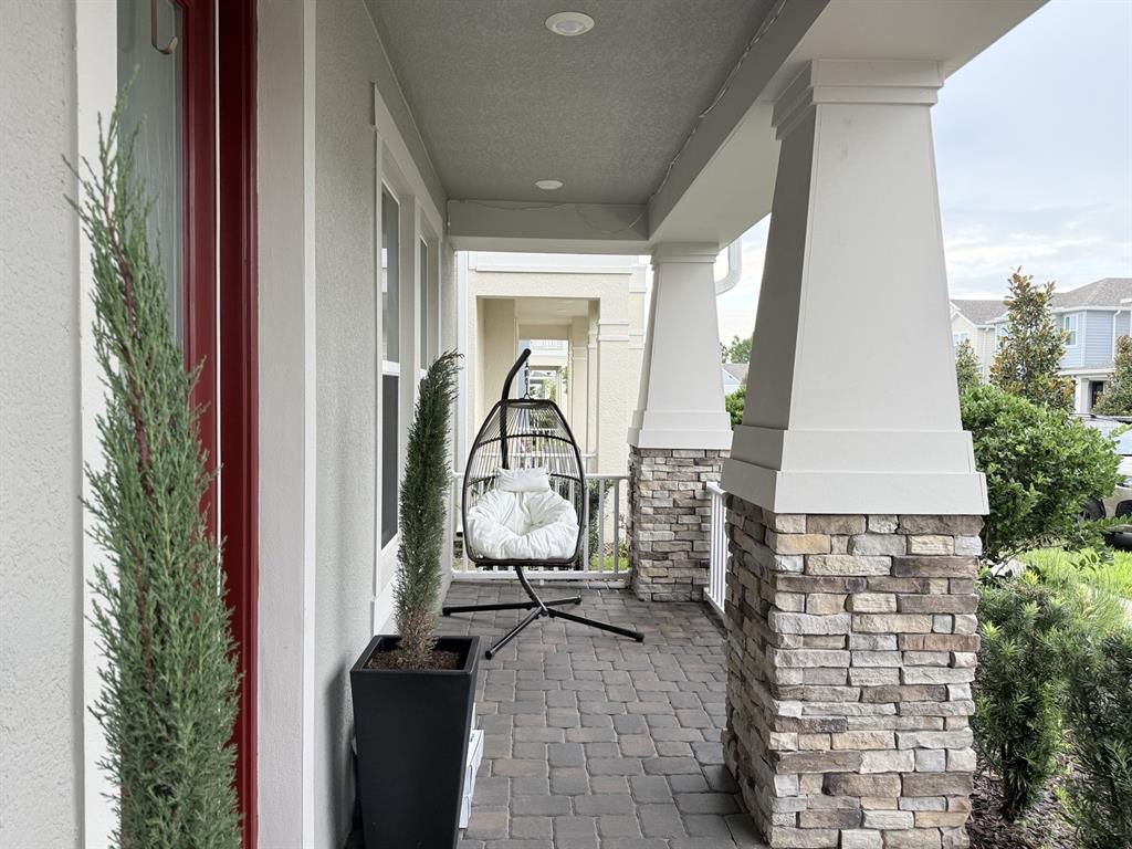 A covered porch features stone-based columns, paver flooring, and a hanging egg chair — 16318 HONEY HARVEST STREET, WINTER GARDEN, FL