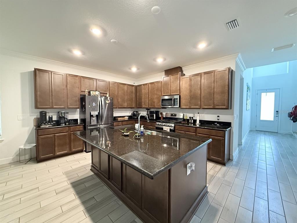 A kitchen with dark wood cabinets, granite countertops, a large island, and light tile flooring — 16318 HONEY HARVEST STREET, WINTER GARDEN, FL
