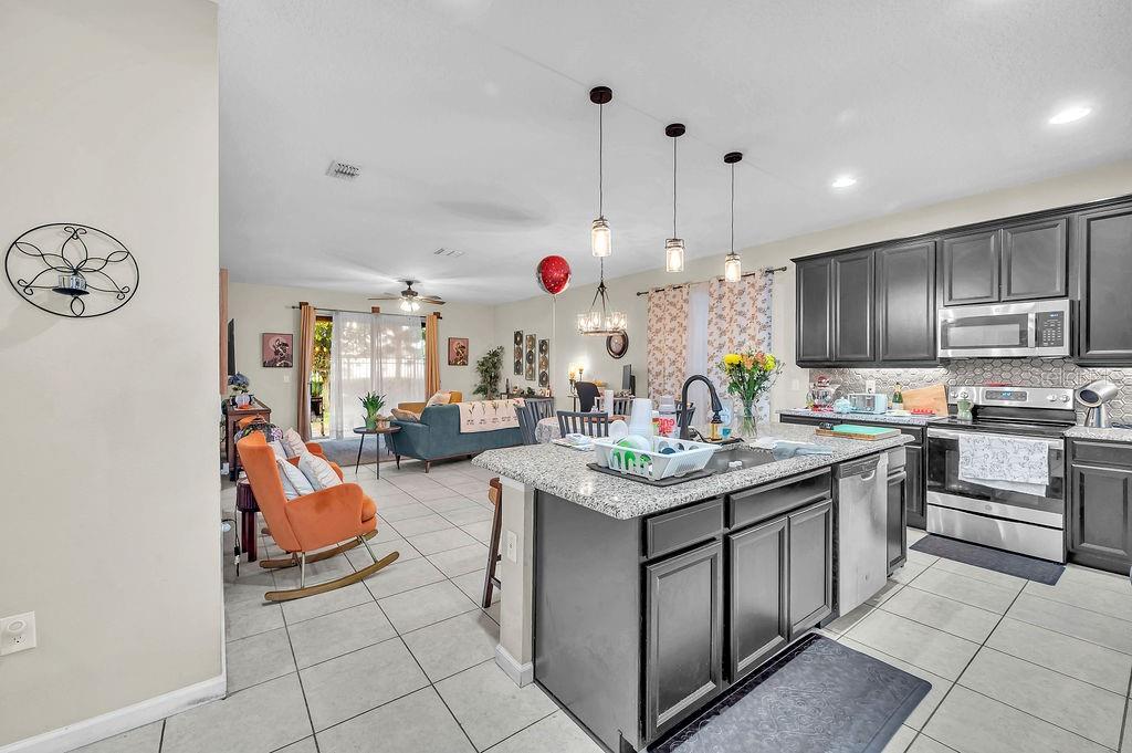 An open-concept kitchen with dark cabinets and granite countertops overlooks a living area with tile — 189 TRINITY RIDGE CIRCLE, DAVENPORT, FL