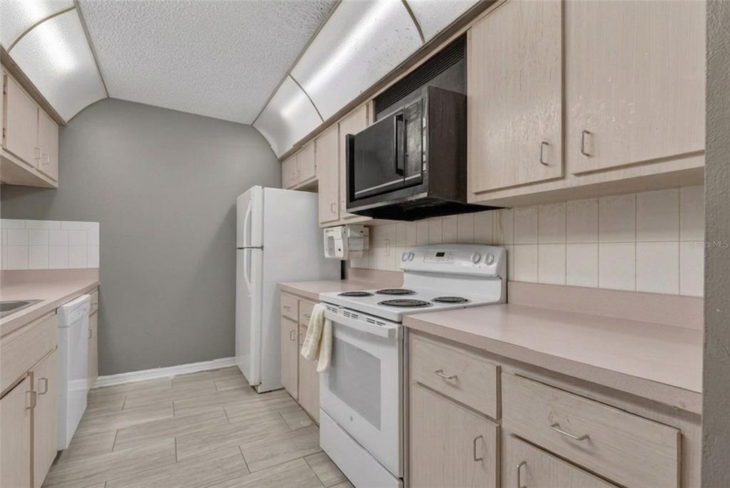 A galley kitchen features light wood cabinets, white appliances, a tiled backsplash, and light flooring — 1826 SW 35TH AVENUE, OCALA, FL