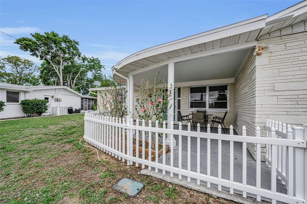 A white brick house features a covered patio enclosed by a white picket fence — 4843 CALAIS DRIVE, HOLIDAY, FL