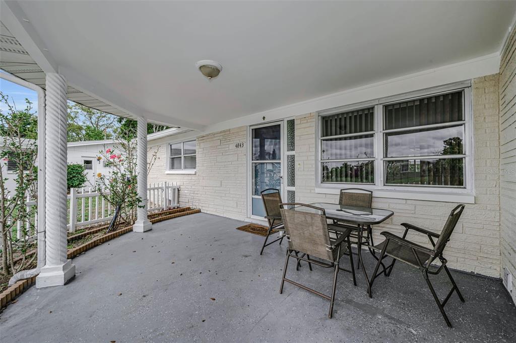 A covered concrete patio features a small glass table with three chairs and white columns — 4843 CALAIS DRIVE, HOLIDAY, FL