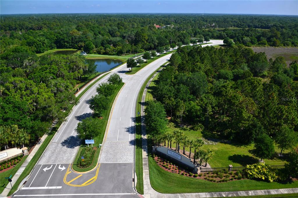 An aerial view shows the entrance to a residential community with a paved road and landscaping — 9255 SWAYING BRANCH ROAD, SARASOTA, FL