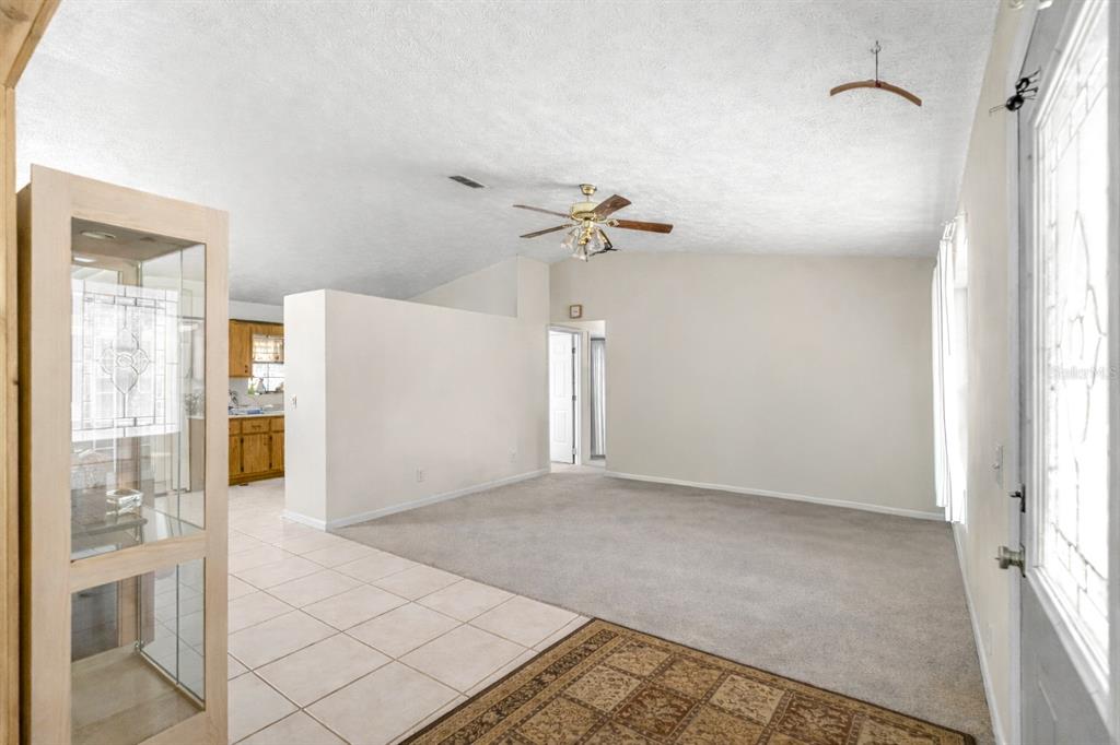 A living room with carpeted flooring, a ceiling fan, and an adjacent tiled kitchen area — 4551 SW 129TH COURT, OCALA, FL