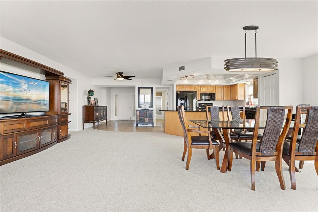 A living and dining area features beige carpeting, a large wooden entertainment center, and kitchen — 101 N MARION COURT UNIT 221, PUNTA GORDA, FL