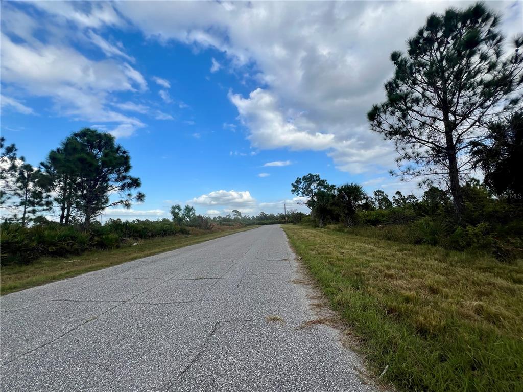 A paved road stretches through a rural area with scattered trees and a blue sky — 12093 GALLOP AVENUE, PORT CHARLOTTE, FL