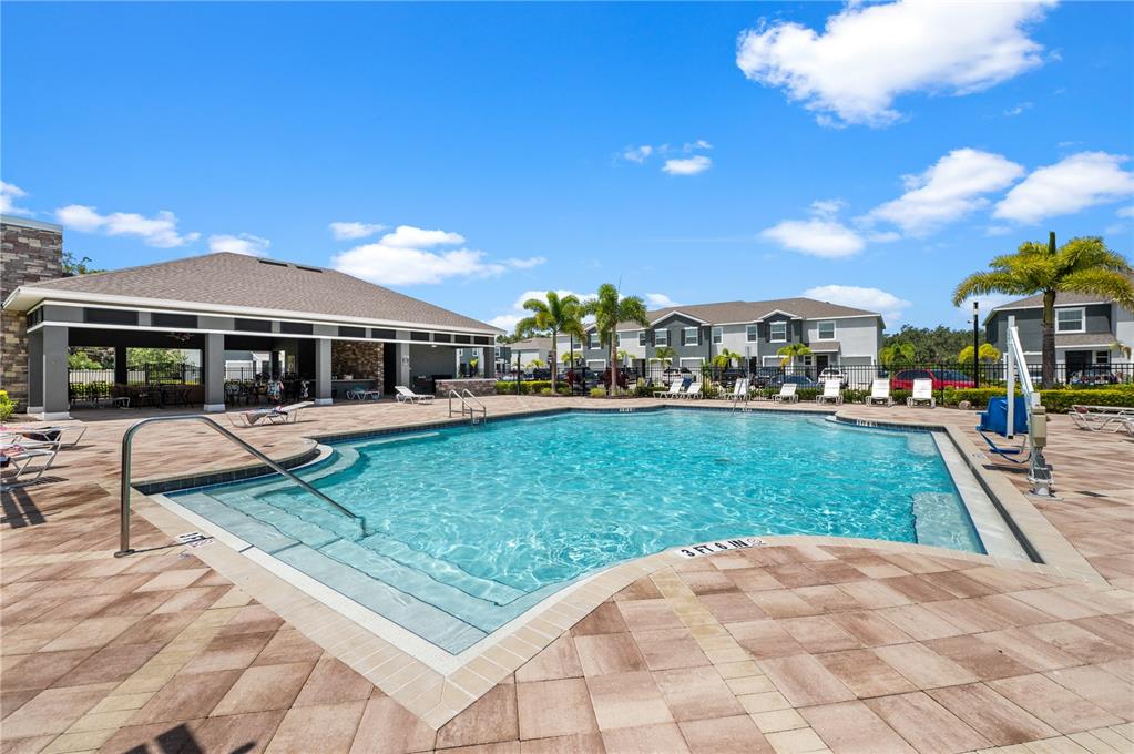 A swimming pool with a covered patio area and surrounding apartment buildings under a blue sky — 8924 MILESTONE DRIVE, SARASOTA, FL