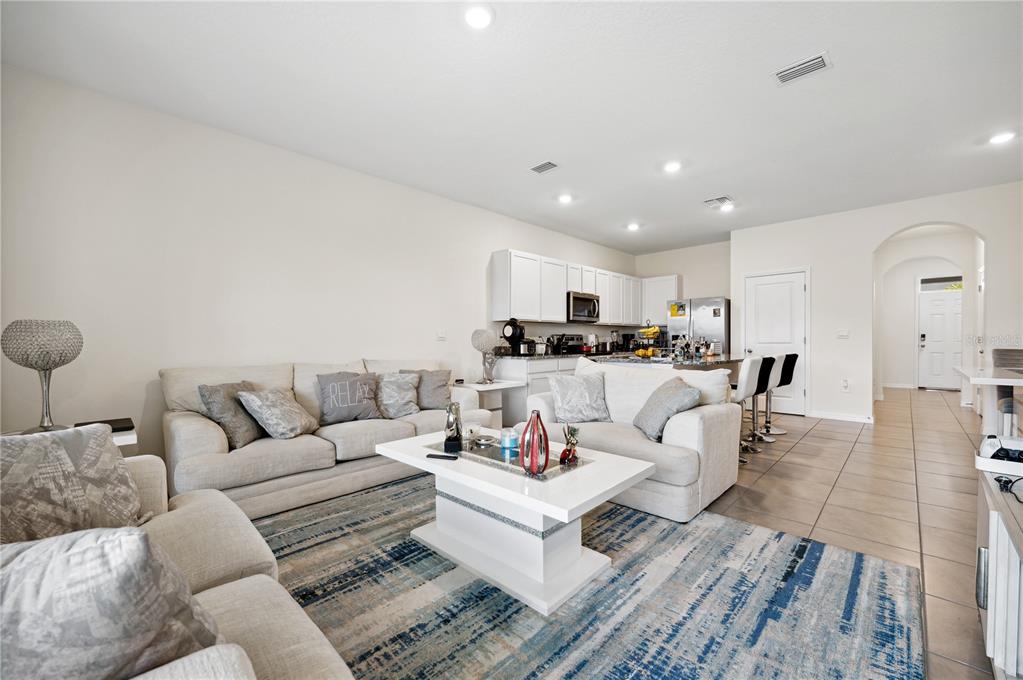 A living room with light-colored sofas, a white coffee table, and an open-concept kitchen — 8924 MILESTONE DRIVE, SARASOTA, FL