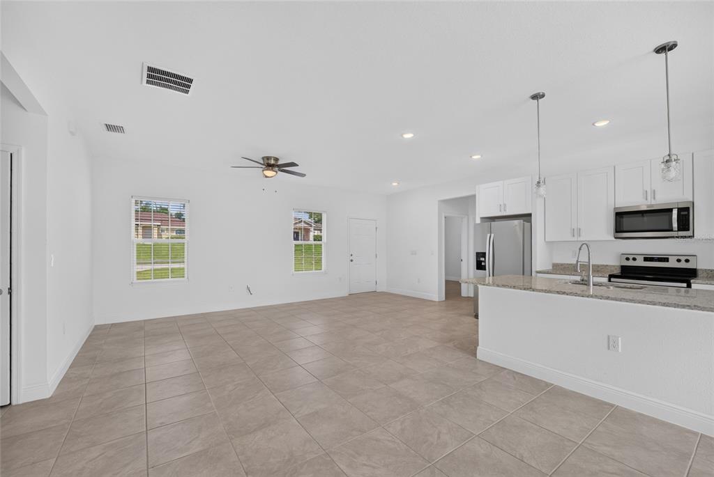 An open-concept kitchen and living area features white cabinetry, granite countertops, and tile flooring — 15475 SW 23RD AVENUE ROAD, OCALA, FL