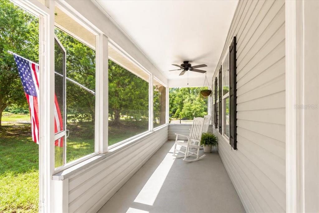 A screened-in porch features white siding, a ceiling fan, rocking chairs, and an American flag — 25419 NW 105TH PLACE, HIGH SPRINGS, FL