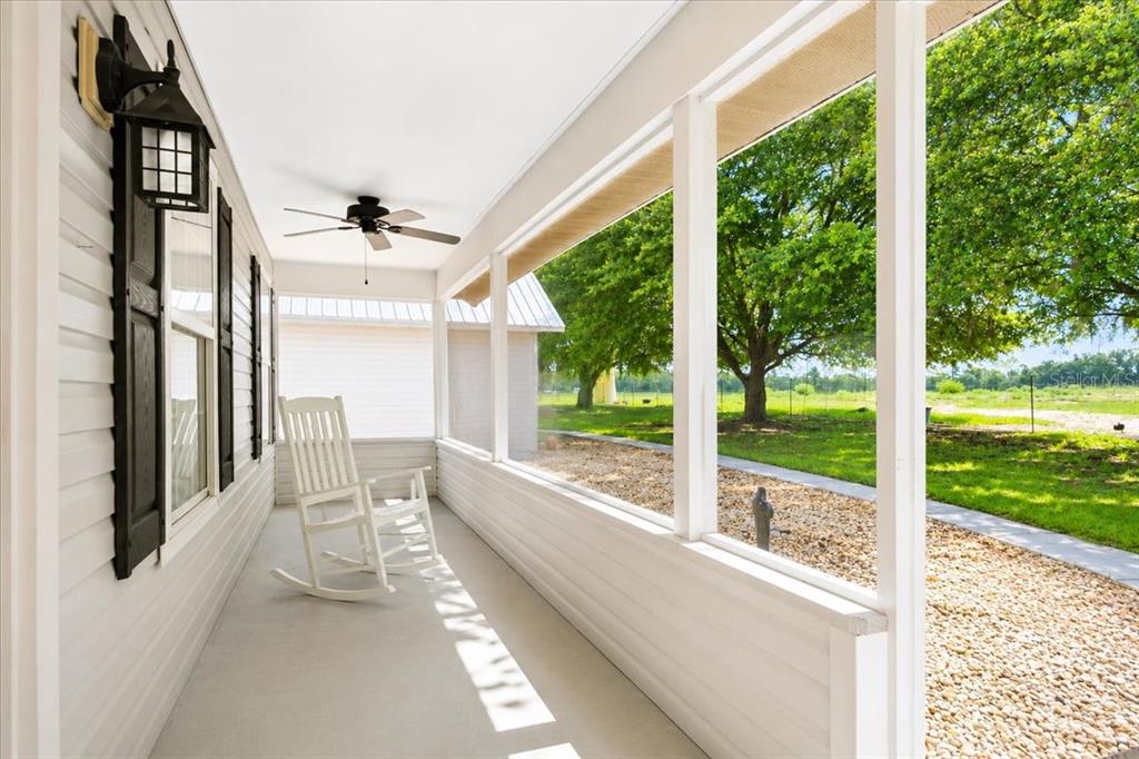 A white screened-in porch features a rocking chair, a ceiling fan, and large windows — 25419 NW 105TH PLACE, HIGH SPRINGS, FL