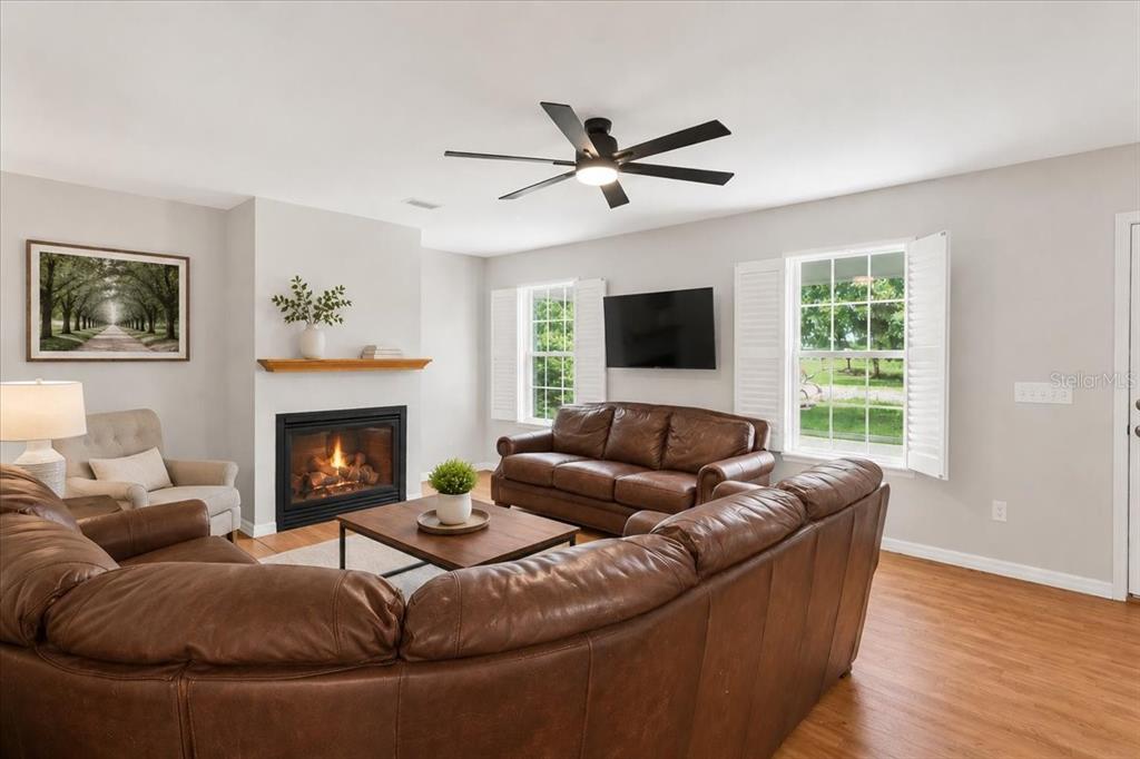 A living room features a fireplace, leather furniture, a ceiling fan, and two windows — 25419 NW 105TH PLACE, HIGH SPRINGS, FL